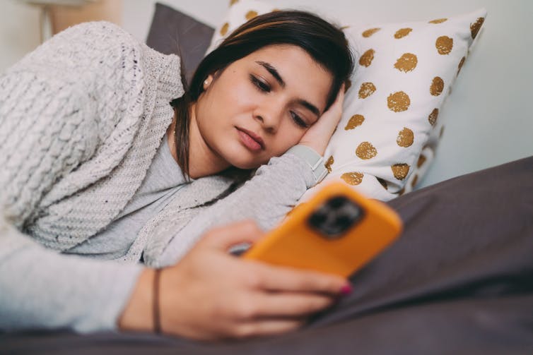 A young woman on her bed is looking at her smartphone.