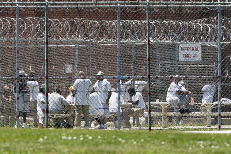 Prisoners populate a yard surrounded by razor wire.