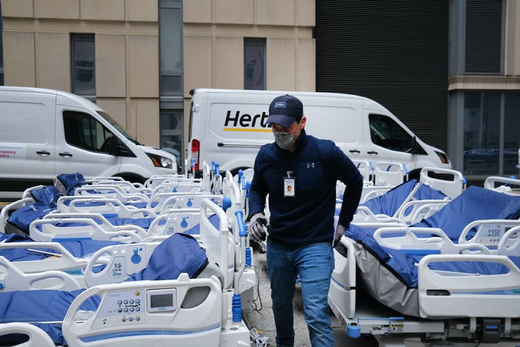 Dozens of medical beds are unloaded at a hospital loading dock.