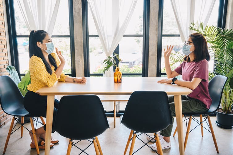 Two woman wave across a table.