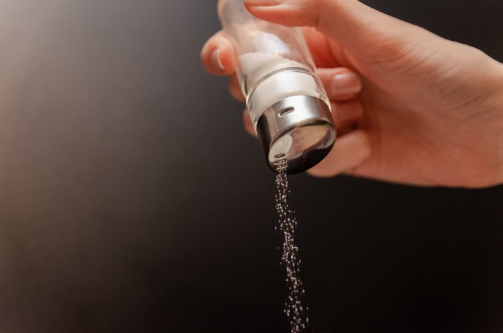 Sprinkle salt from a jar on a black background. Hand with a can of salt on a black background