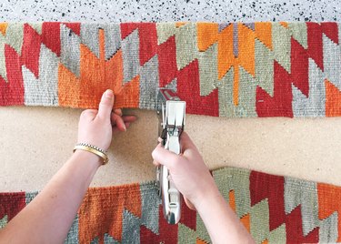 Staple center point of rug on long sides of the bench