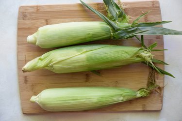 3 corn on the cobb on a cutting board.